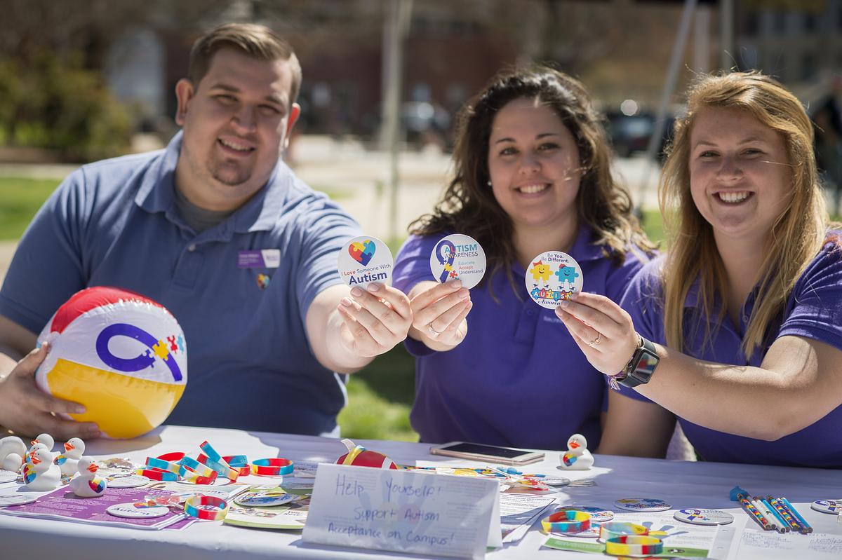 Autism awareness booth with staff holding up pins smiling for the camera