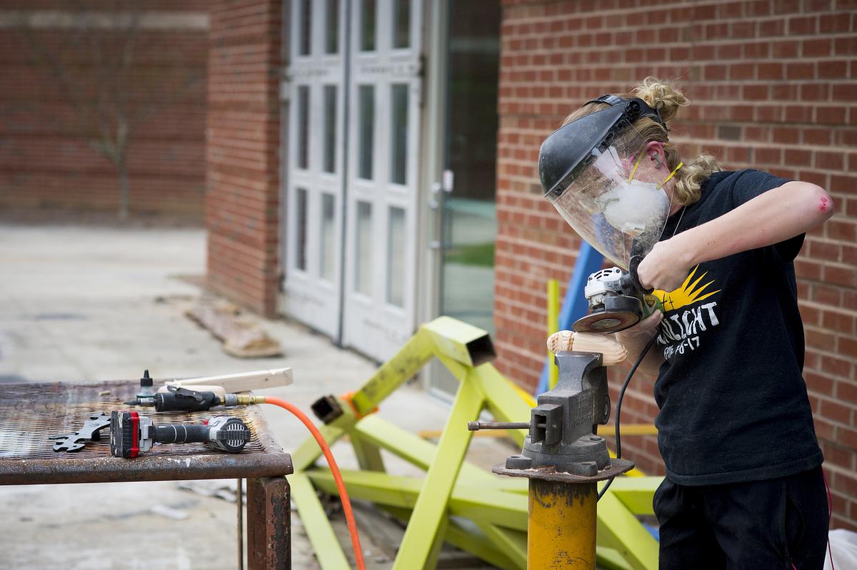 Student with face shield and power tools working on a sculpture project