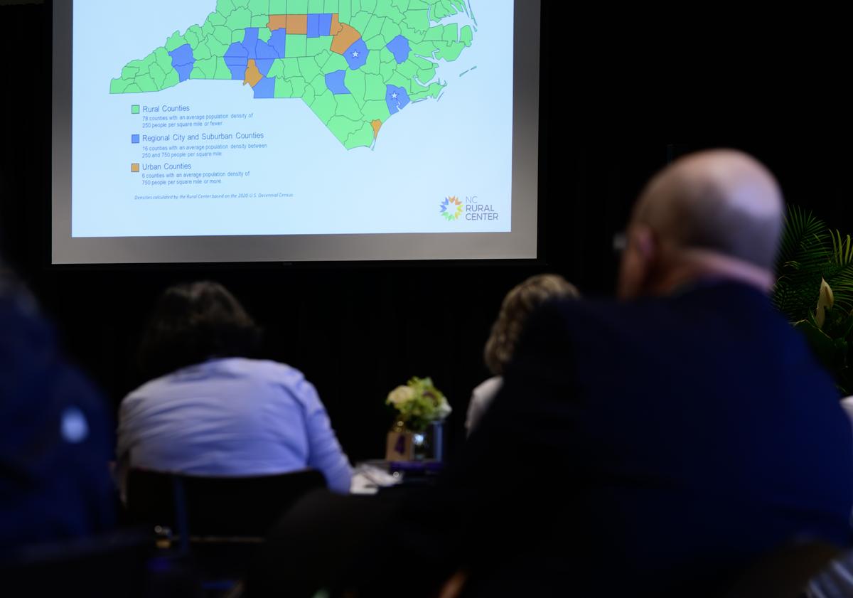 Audience listening to a lecture with an image of North Carolina on a screen highlighting specific counties 