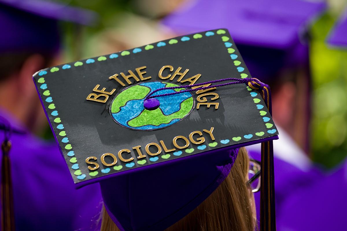 A student during the graduation ceremony wearing a cap the says "Be The Change - Sociology"