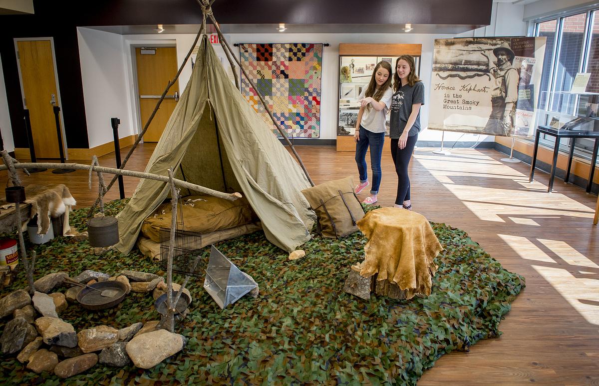 Historic canvas tent on display with two visitors viewing museum exhibits about frontier life and quilts.