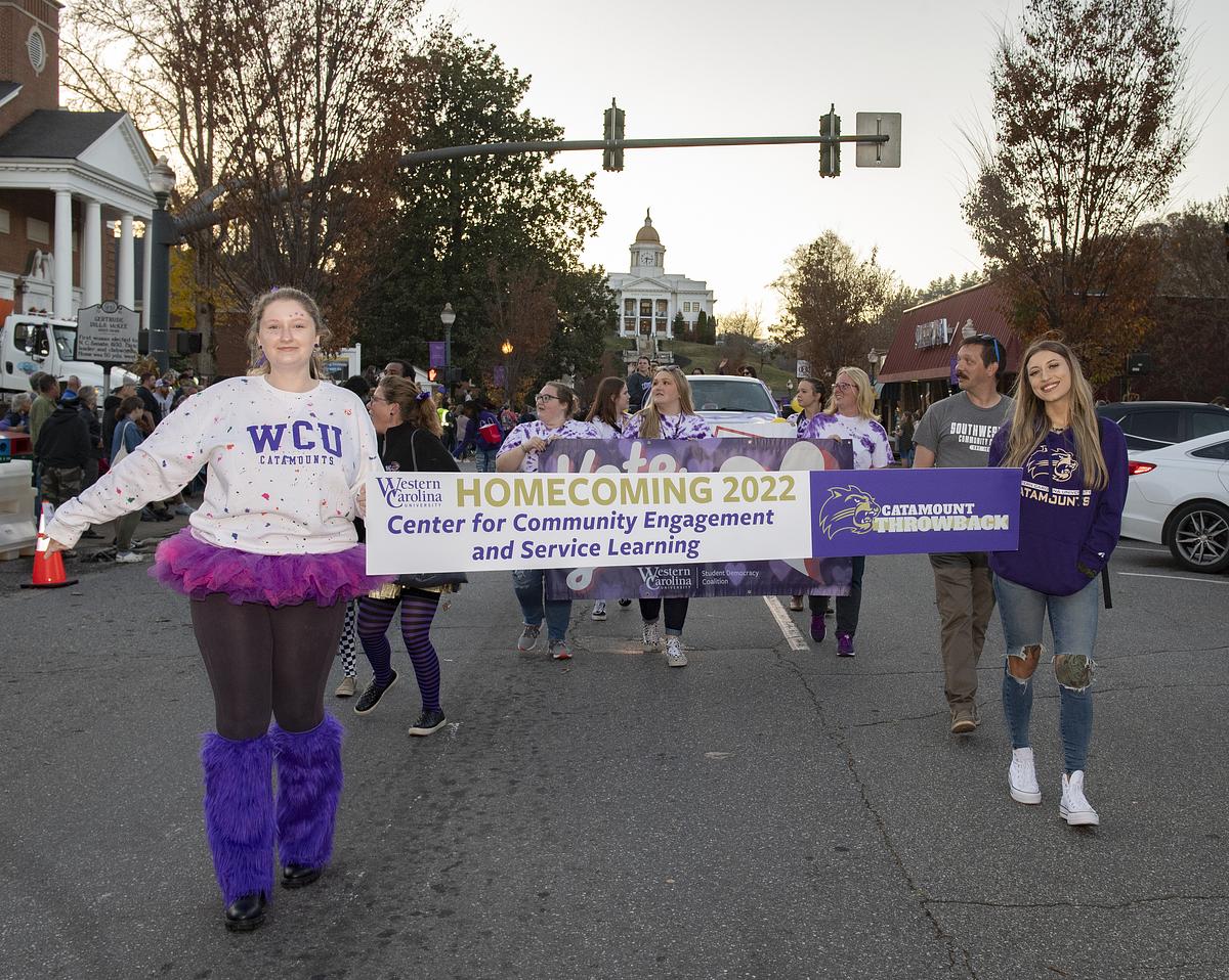 Students marching the the homecoming parade holding up a Community Engagement Banner