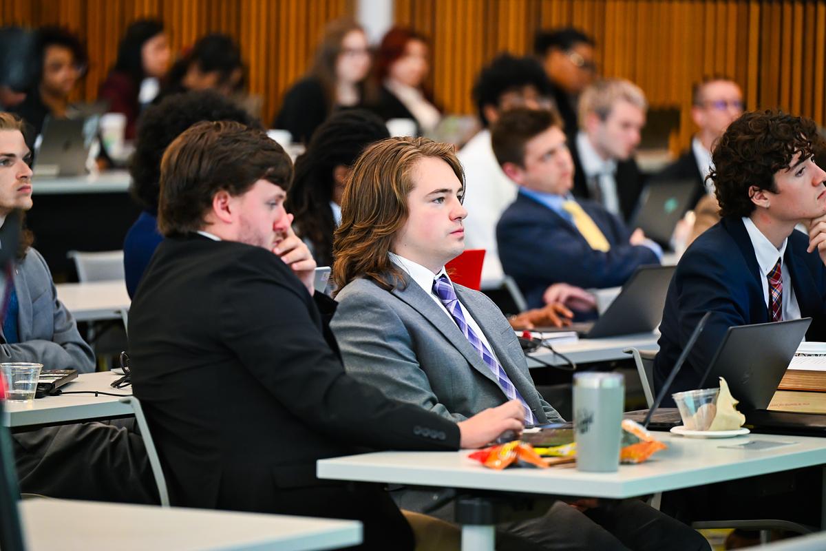 Students dressed in suits, sitting at desks as they listen to a lecturer