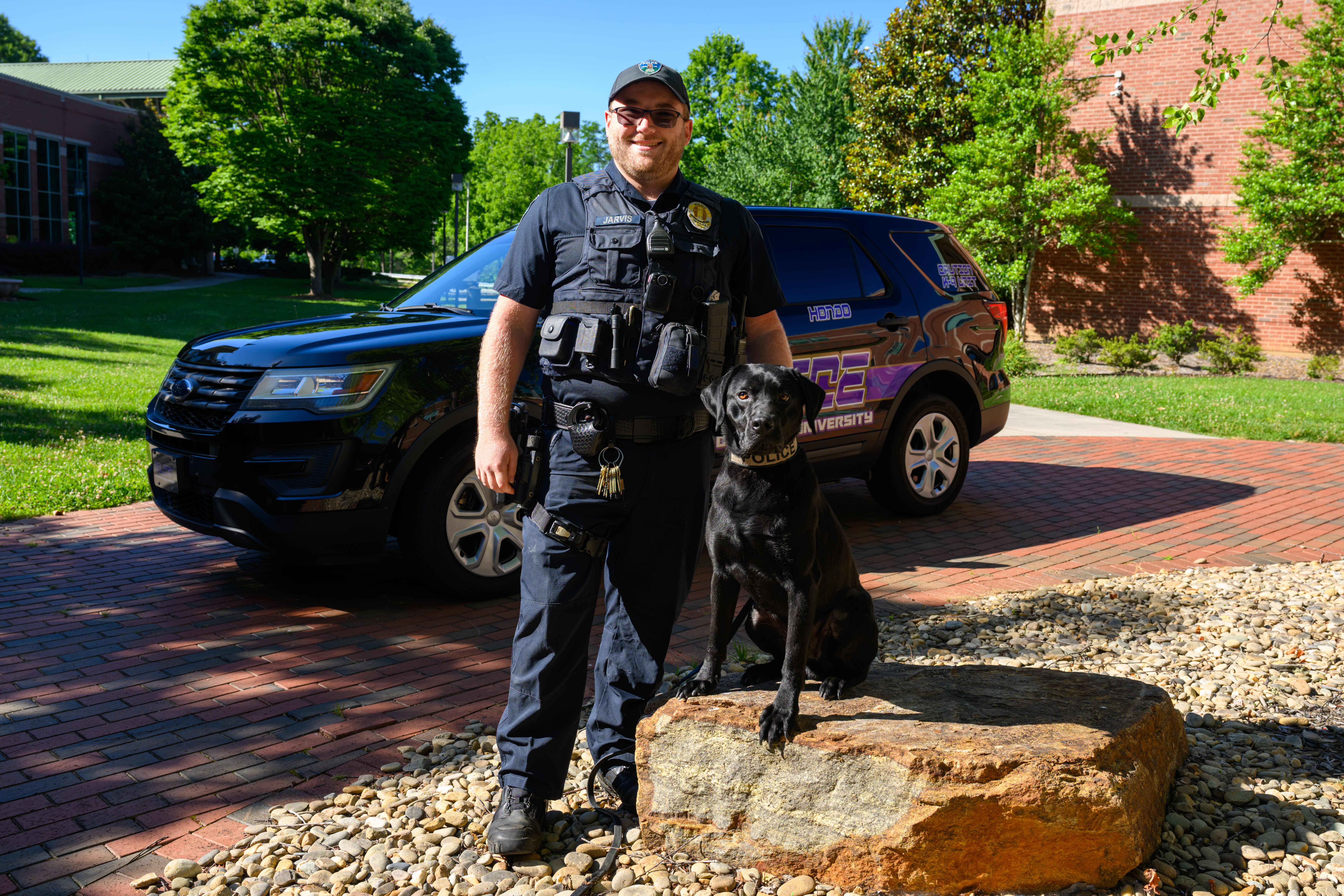 WCUPD officer Anthony Jarvis stands next to K-9 dog Hondo in front of a campus police car.