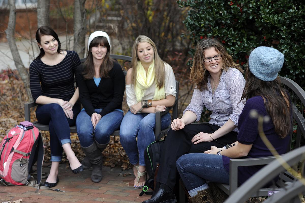Faculty and students sitting at benches outside on campus