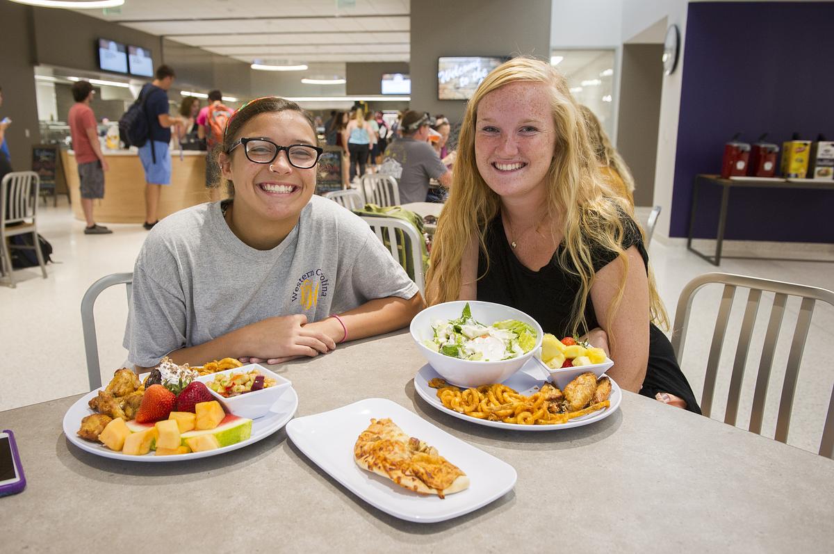 Two students sitting together smiling for the camera with a wide variety of food on the table in multiple dishes