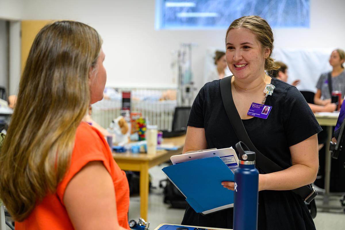 Student practitioner holding a clipboard in a medical lab smiling and talking with someone