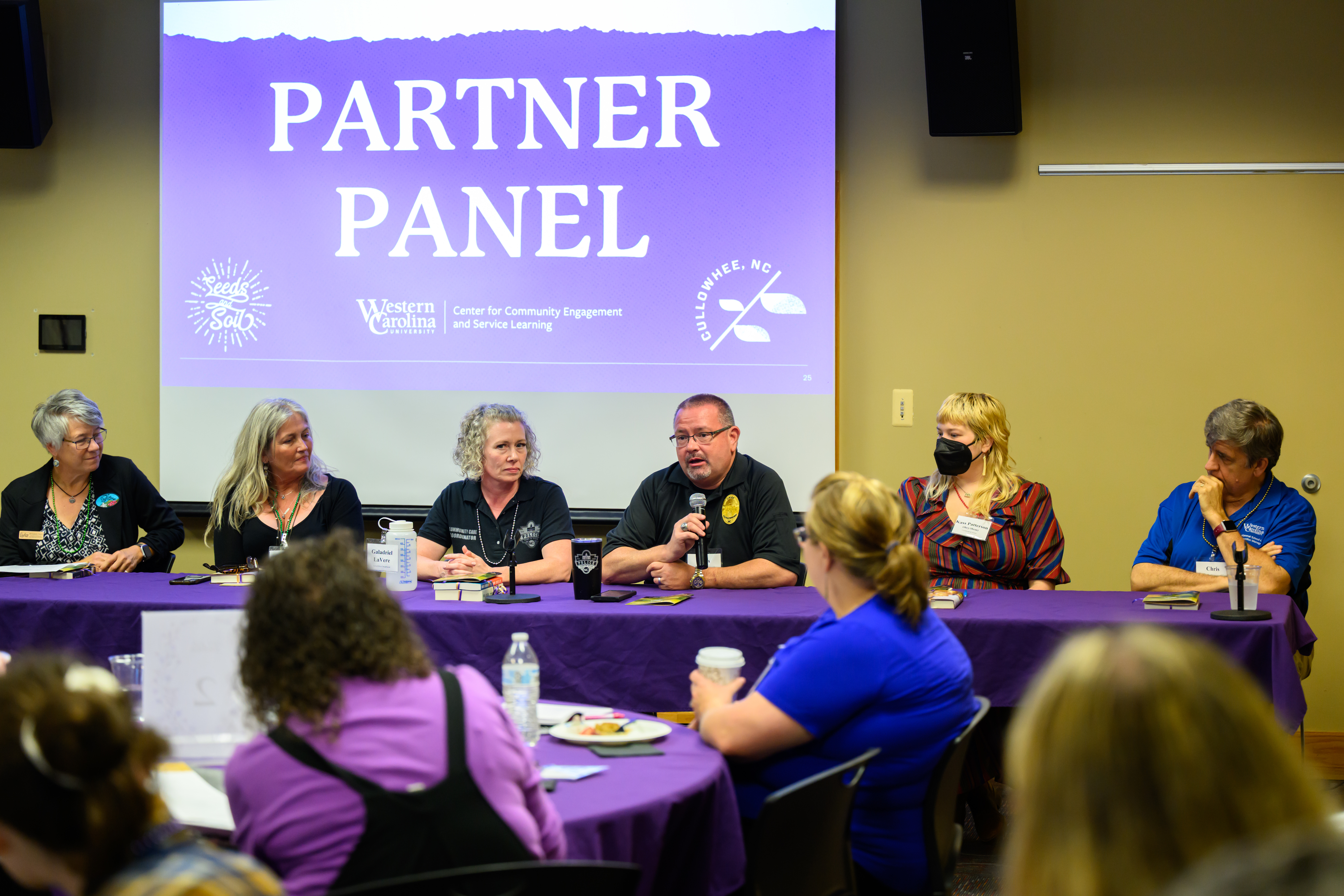 A group of people gathered at a table in front of an audience taking turns to speak