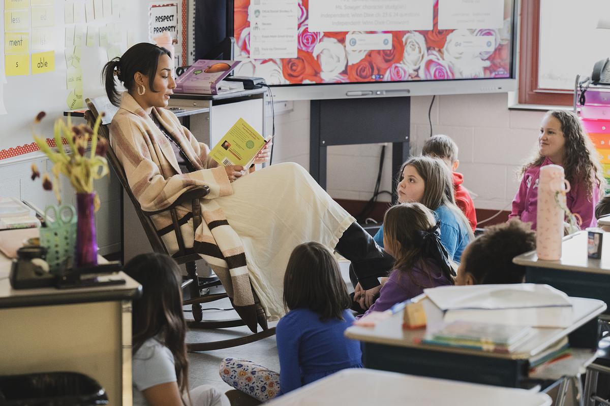 A teacher reading a book in a rocking chair with students in a classroom