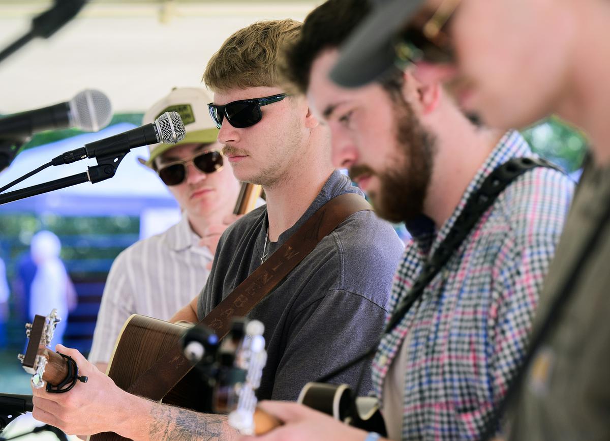 Band of four musicians performing live with microphones, guitars, and stage lighting equipment visible