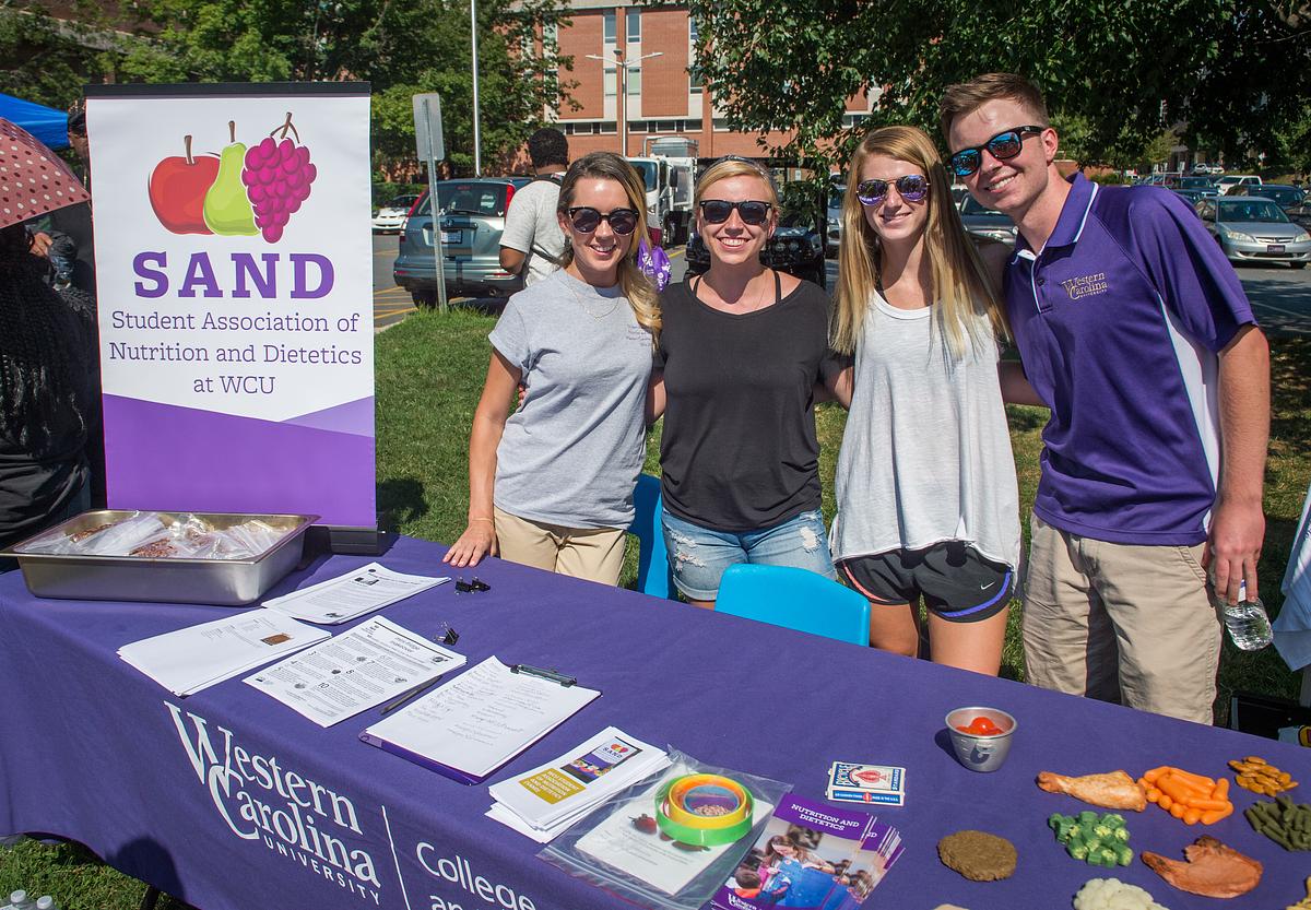 Students of the SAND program smile for the camera together at their stand at a fair