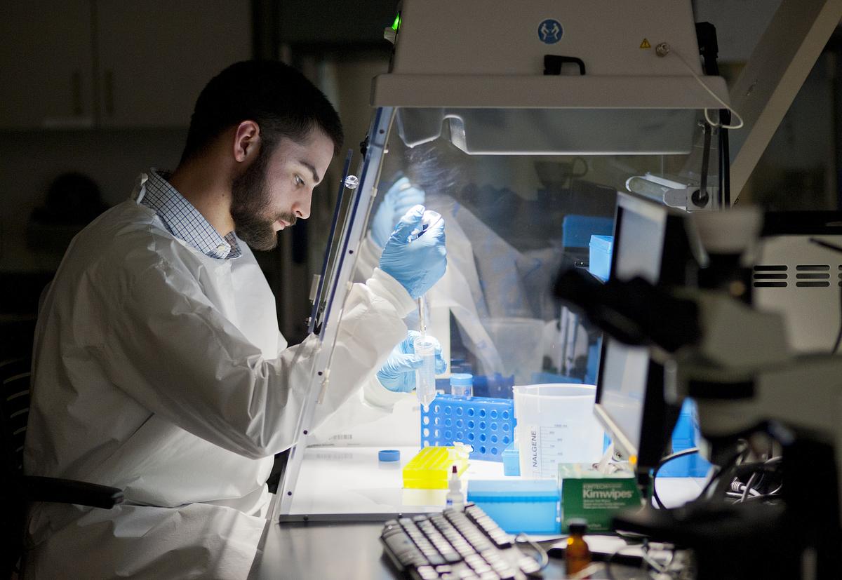 Student in a lab wearing a suit and protective gear working at a table over a microscope