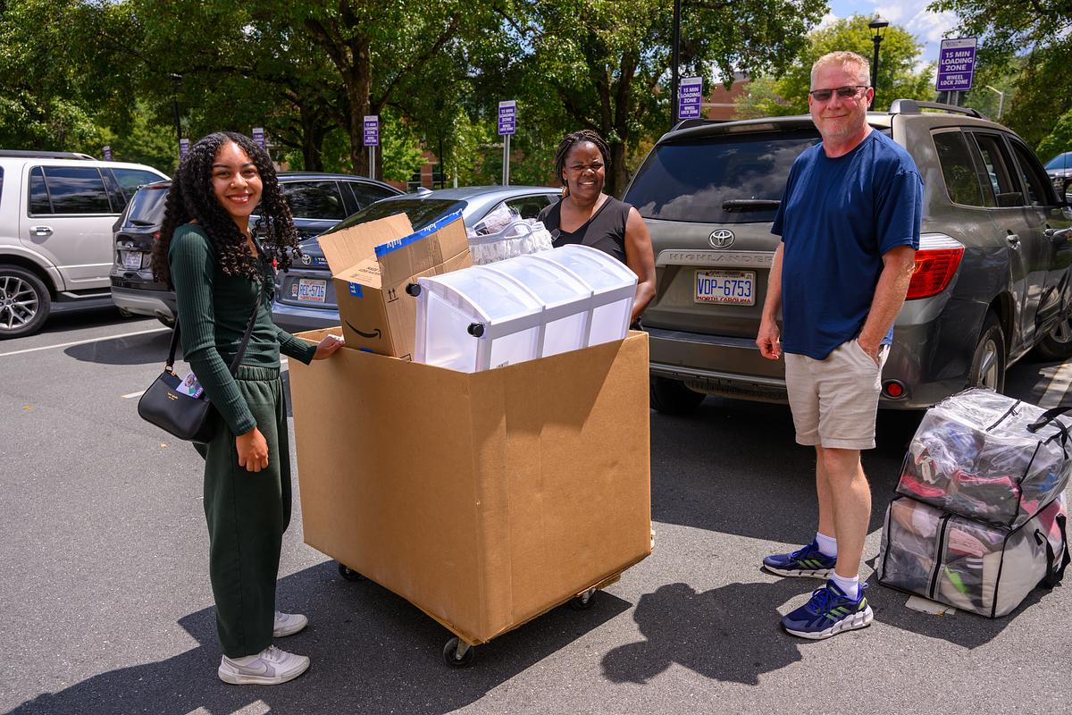 Family standing outside in a parking lot smiling for the camera next to their vehicle
