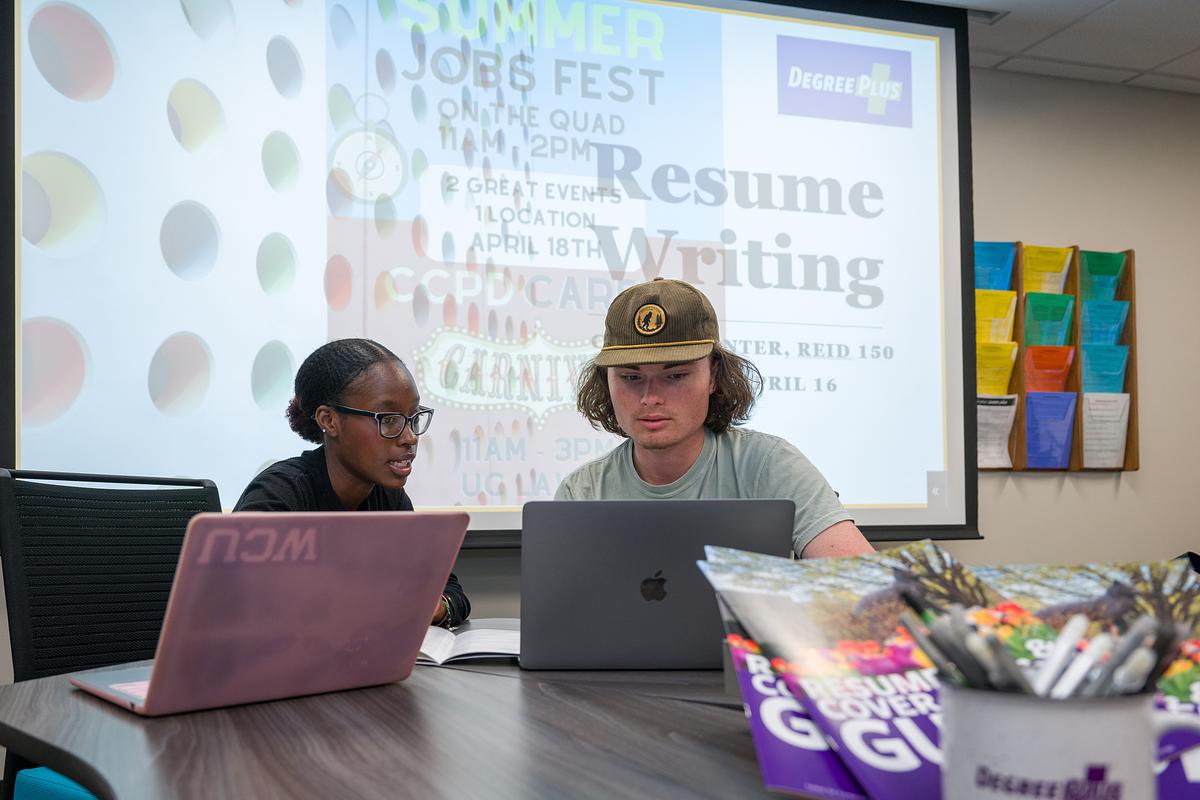 Young black woman talking with a young white man at a table with laptops