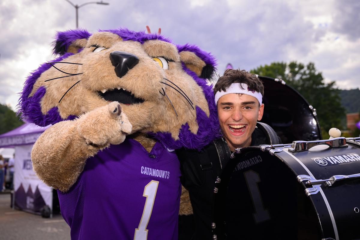 Man in white headband smiling next to purple catamount mascot wearing number one jersey