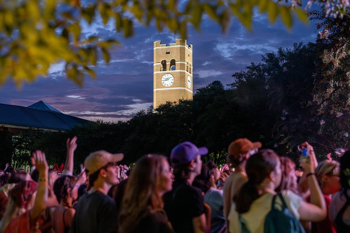 Students gathered in a crowd at sunset with the Alumni Tower glowing in light