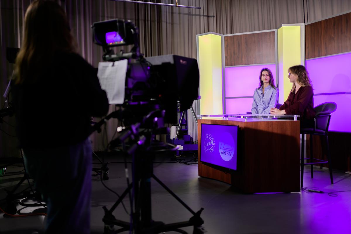 Students sit behind a news desk in the newly renovated WHEE-TV studio