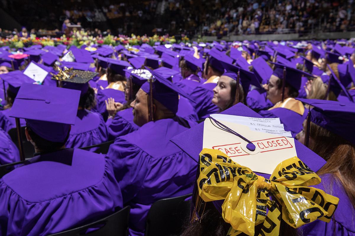 Students sit at the graduation ceremony, with one cap containing a ribbon made of caution tape and file that says case closed