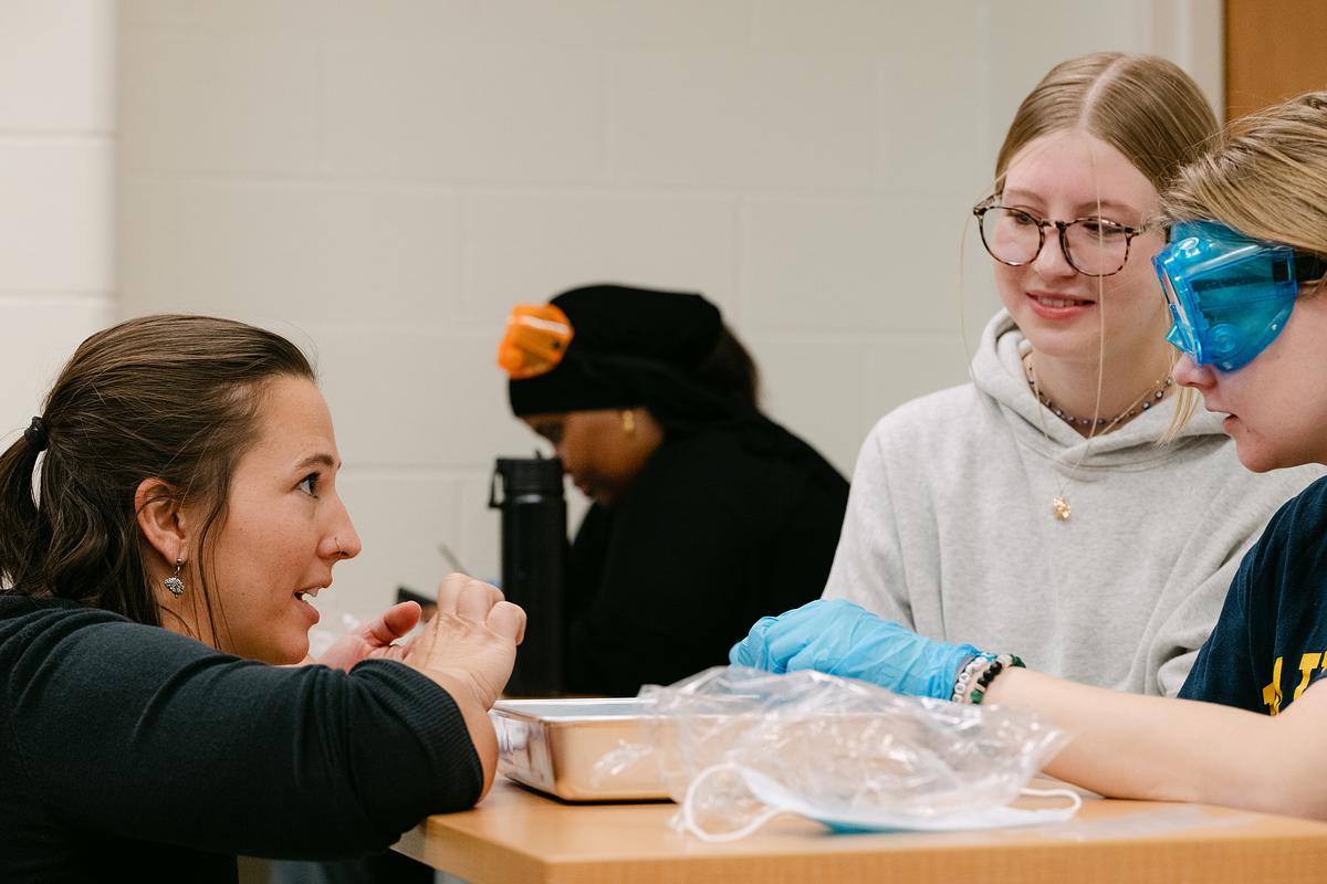 A professor leaning over a desk helping students dissect a brain in a Neuroscience class
