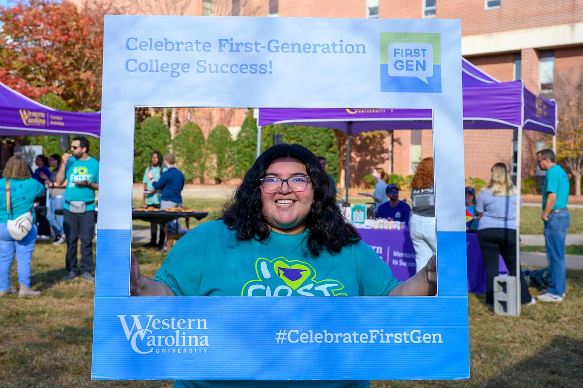 Student holding up First Gen photo frame while wearing I HEART FIRST GEN DAY t-shirt
