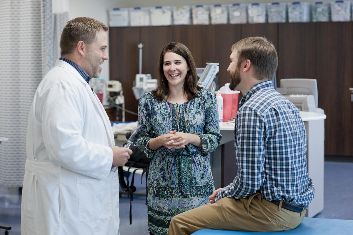 Doctor, nurse practitioner, and patient talking and laughing together in a hospital room