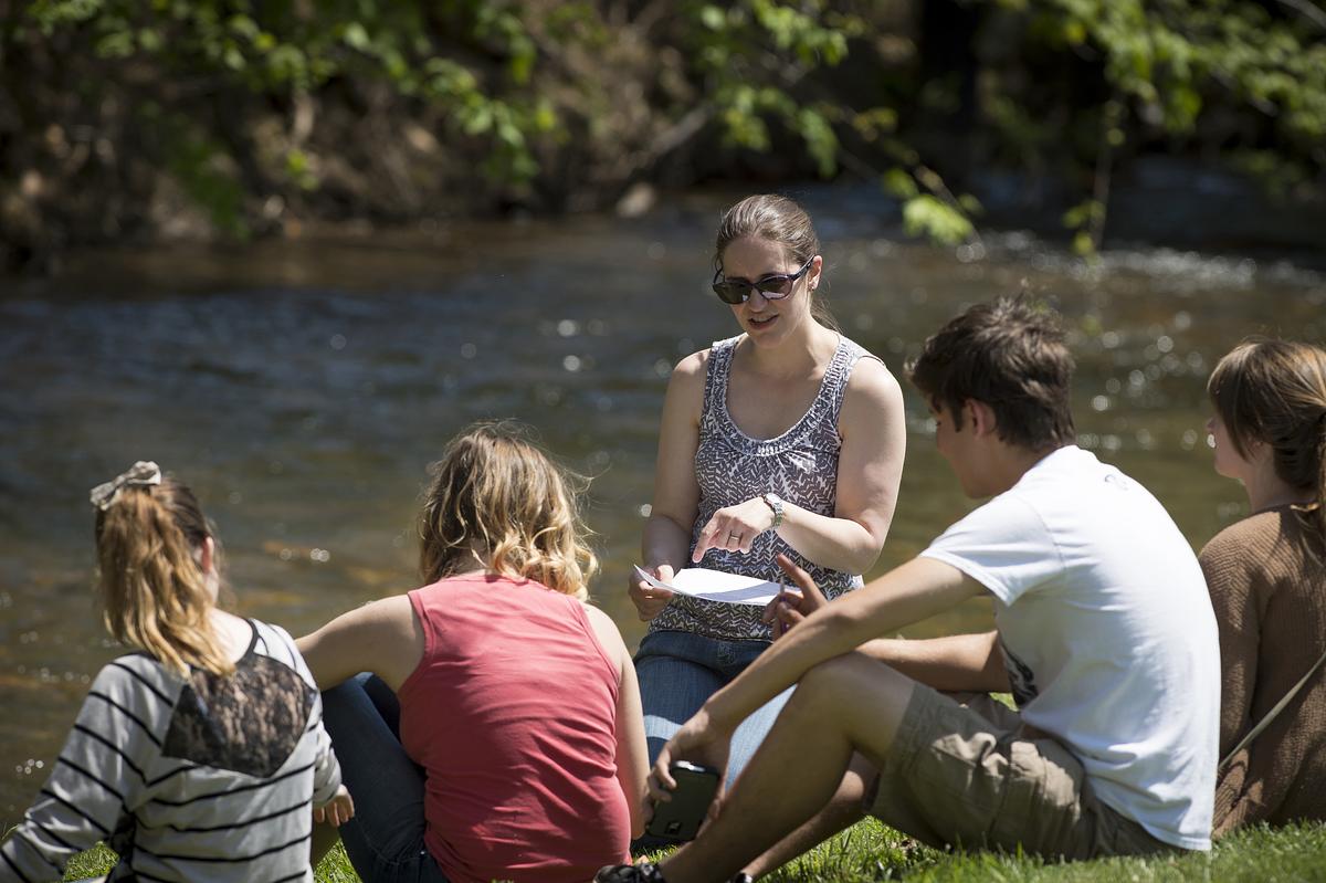 Instructor reading from a document to students by a river