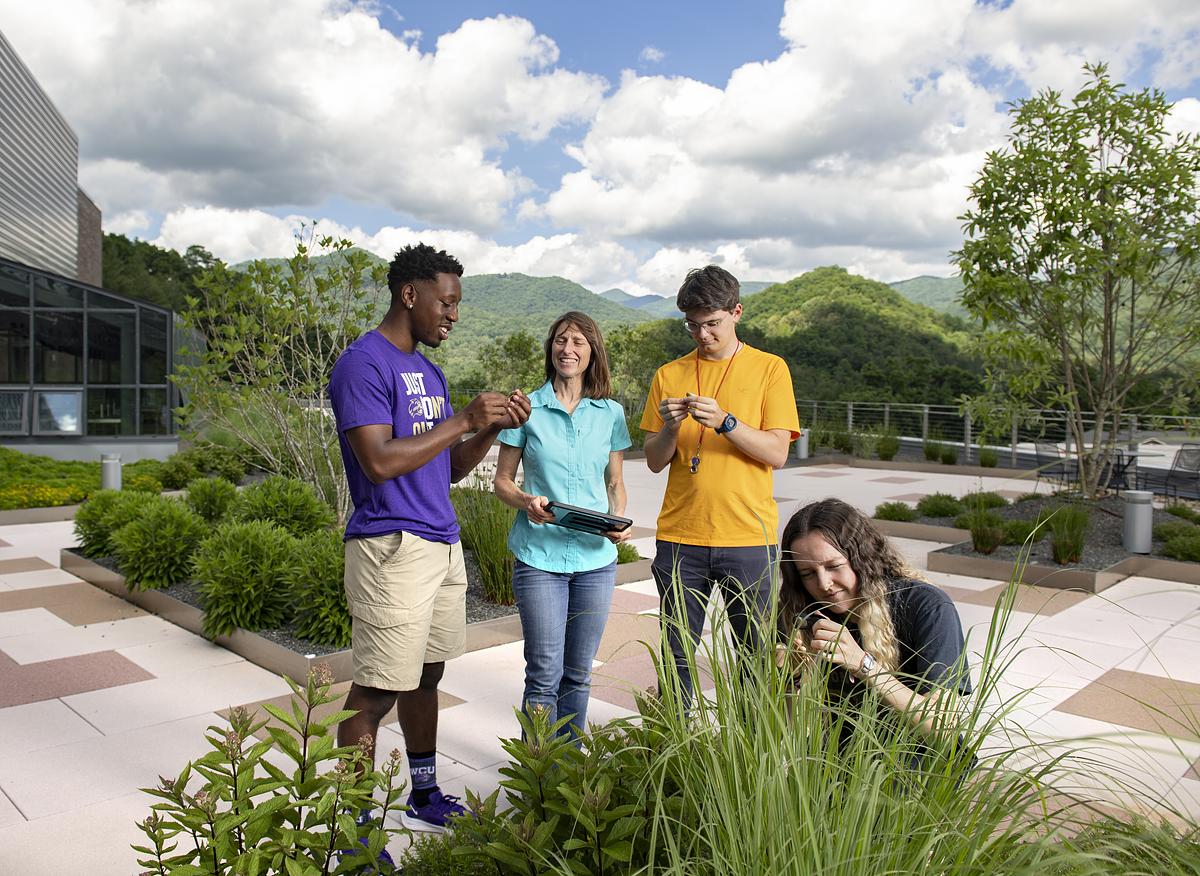 Students and a teacher outside on a terrace observing a variety of plants