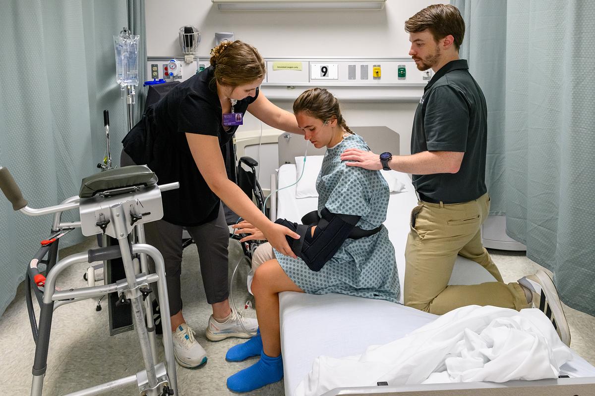 Student help a simulated patient get up from the hospital bed