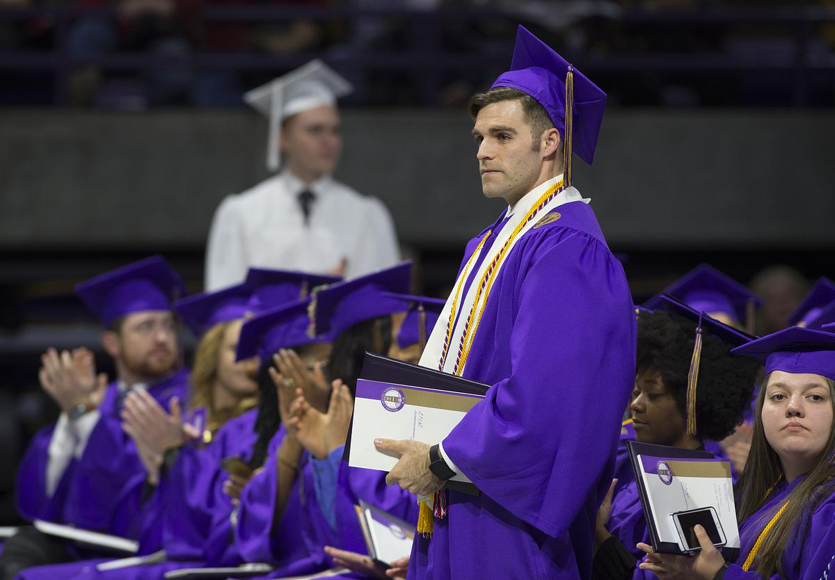 Graduating student standing for commencement in the audience with a diploma