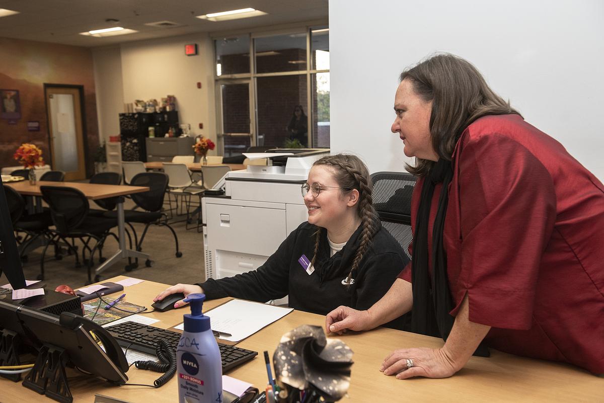 Supervisor leaning over student employee looking at a computer