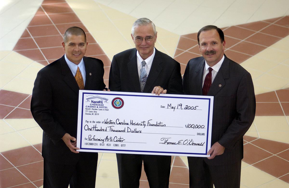 Three men stand together holding a large check for a photo
