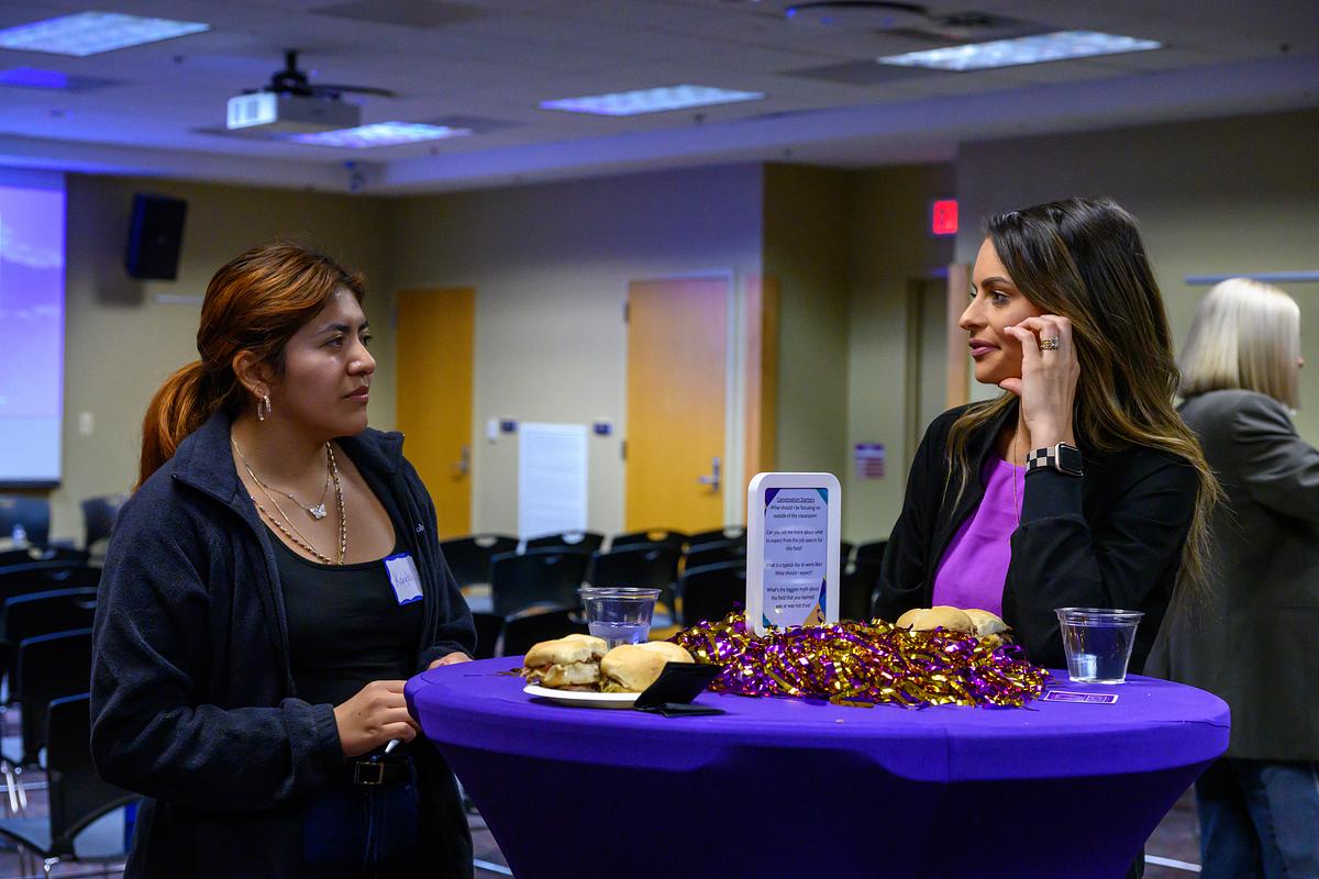 Student speaking with alumni panelist over light refreshments