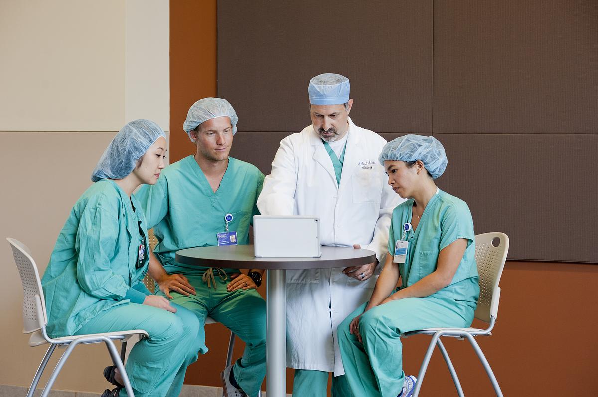 A doctor showing three nursing practitioners something on a laptop screen on a table