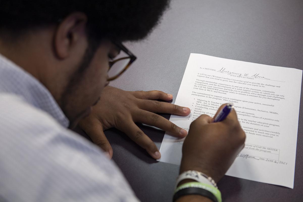 Student signing a document at a table