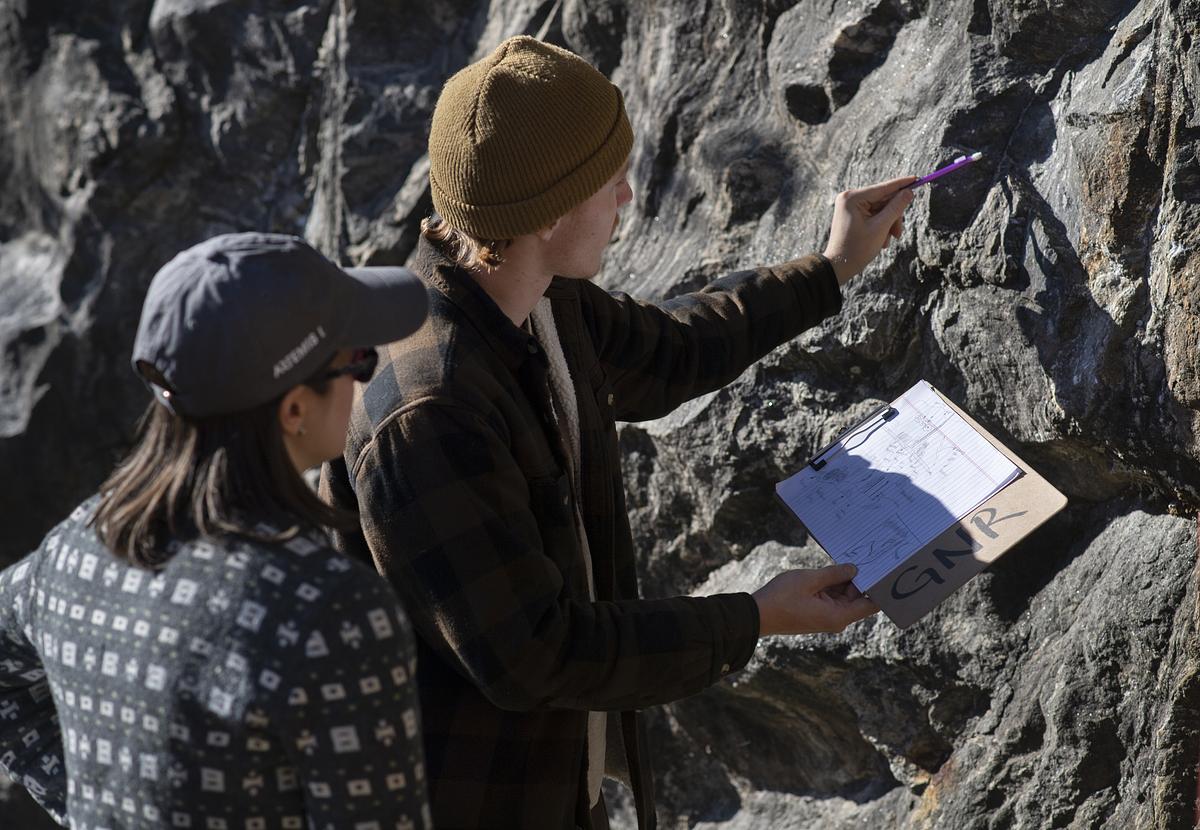 Two people looking over a document on a clipboard pointing toward a rock formation