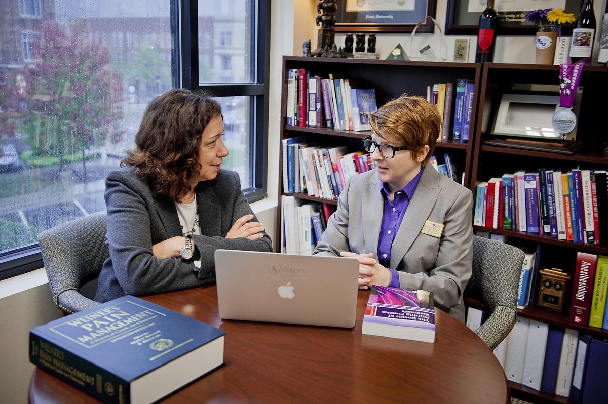 Two teachers at a table in discussion over an open laptop