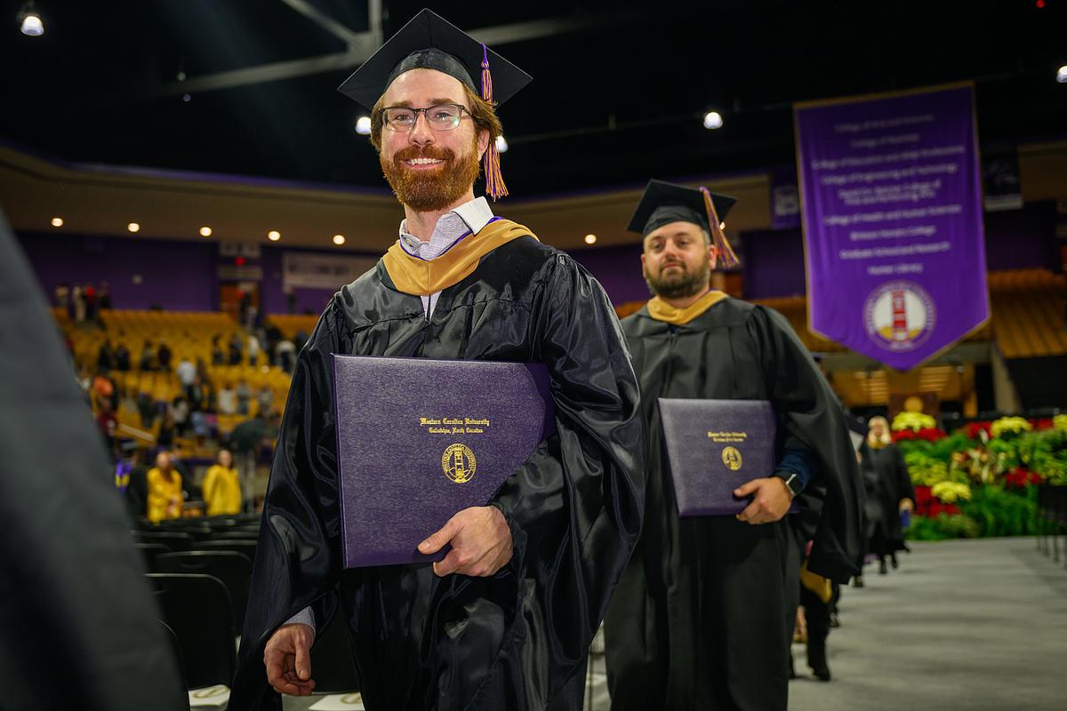 Graduating students at commencement smiling for the camera with their diplomas 
