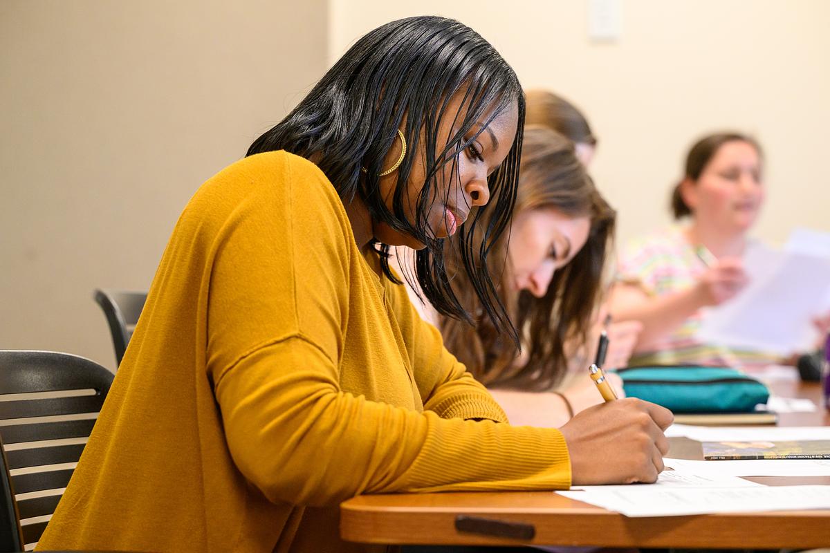 Students focused at a long desk together writing information down