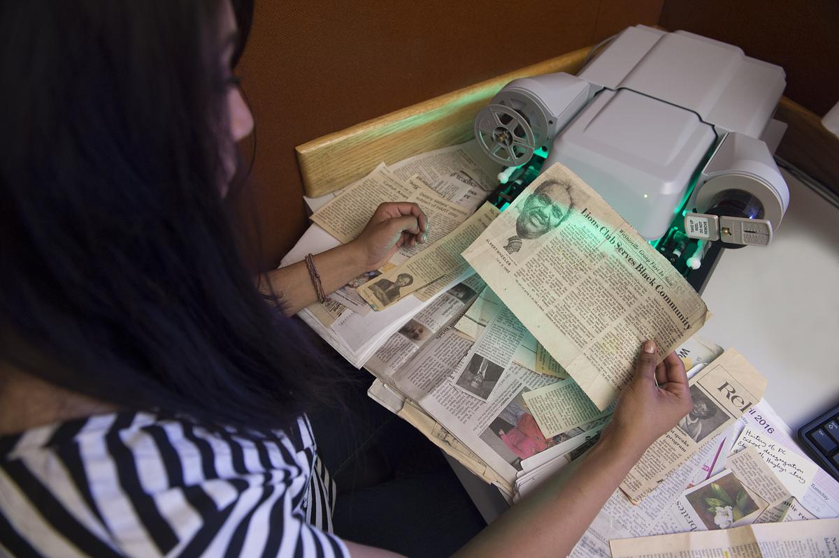 Public history student holding up a variety of old magazine articles under a light