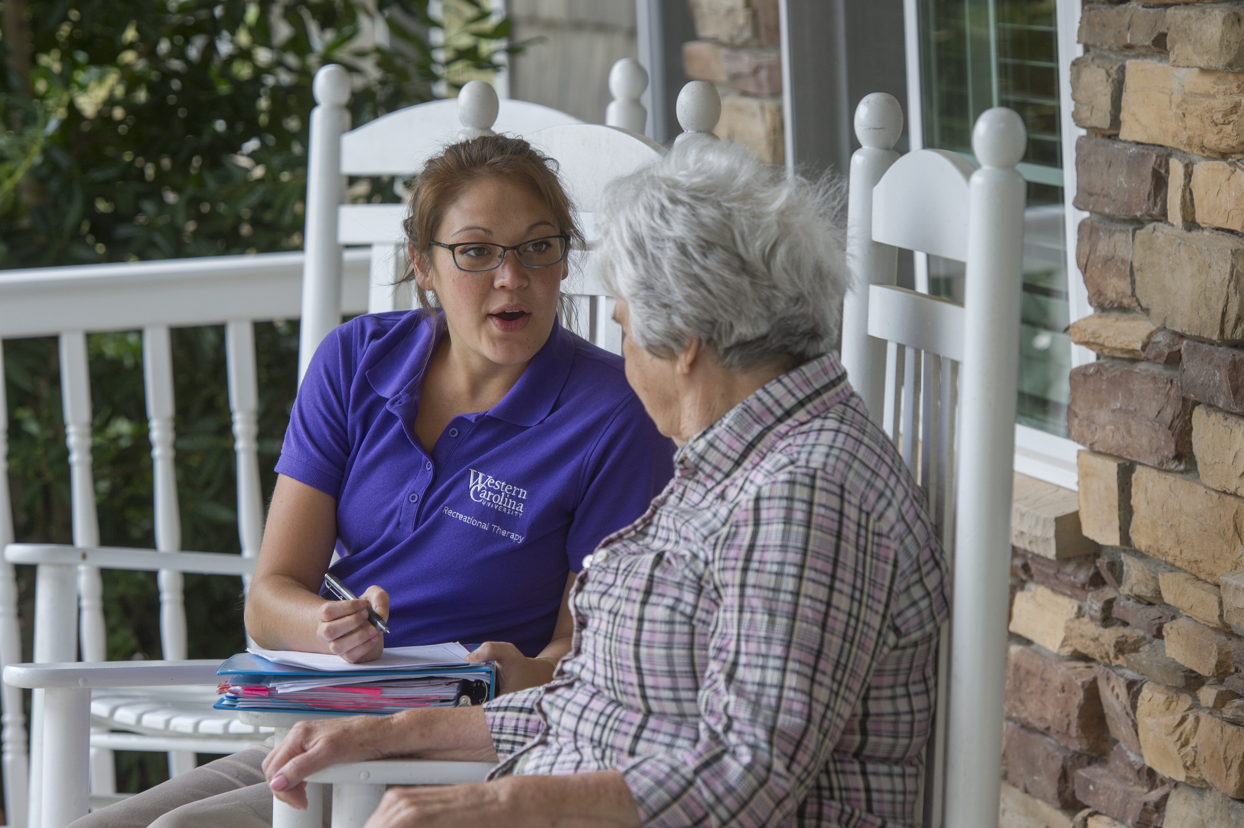 Catamount talks with a senior citizen on a porch in rocking chairs