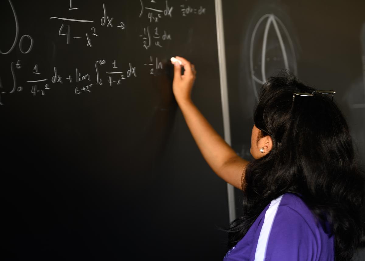 Student solving and writing out a math equation on a chalkboard