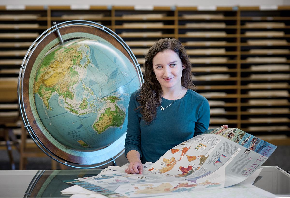 Student reaches out and spins a globe on top of a bookcase