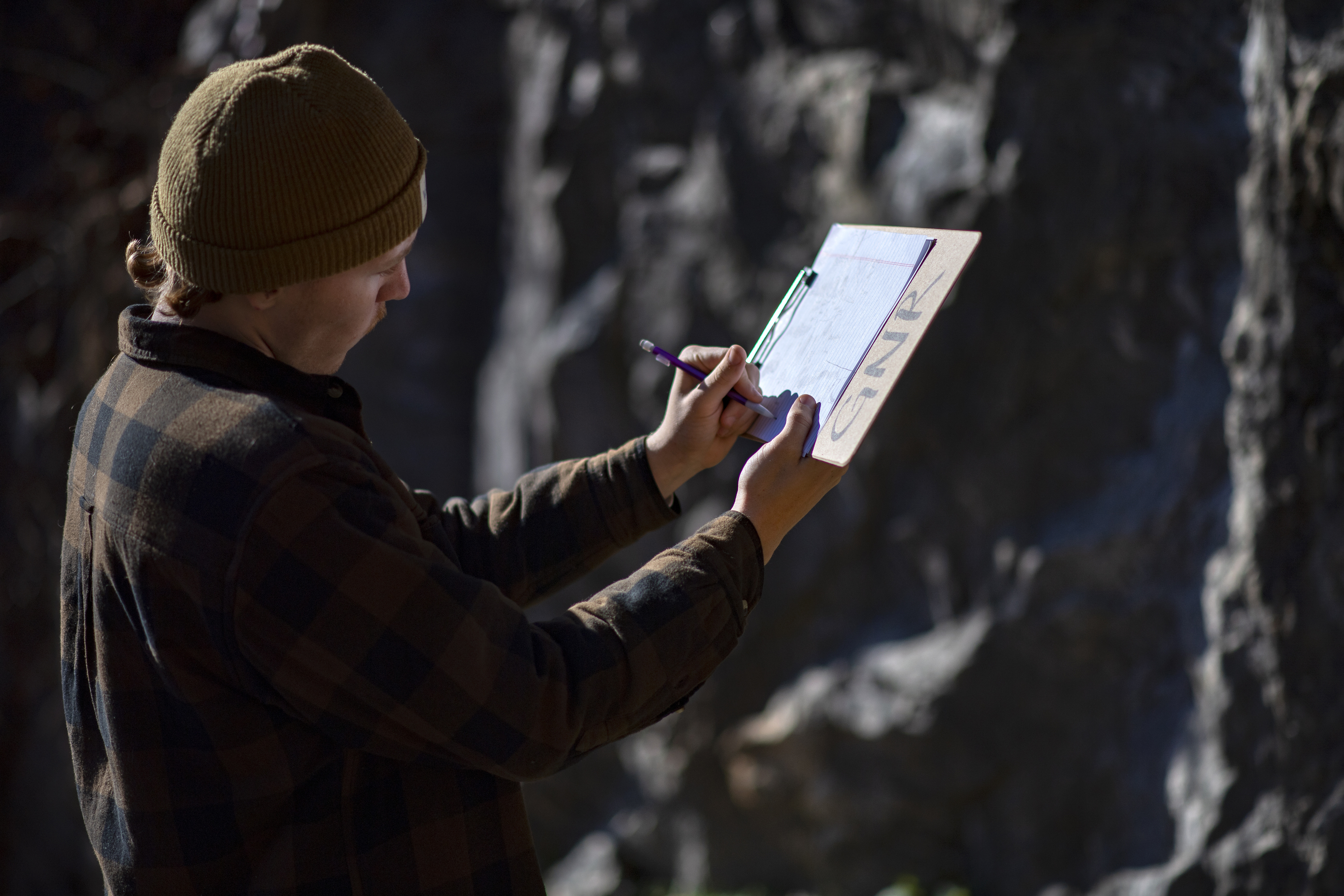 Student observing a rock formation while taking notes on a clipboard