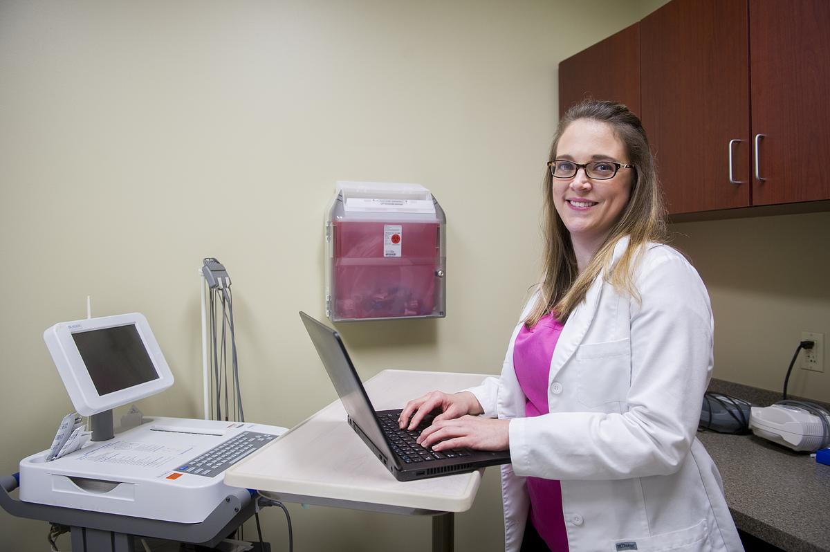 Student nurse Carrie Saunders working on a laptop in a hospital room smiling for the camera