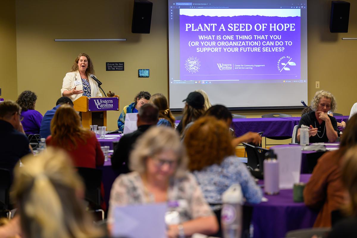 Speaker talking in front of a group of people with a projector on a screen displaying "Plant a Seed of Hope"