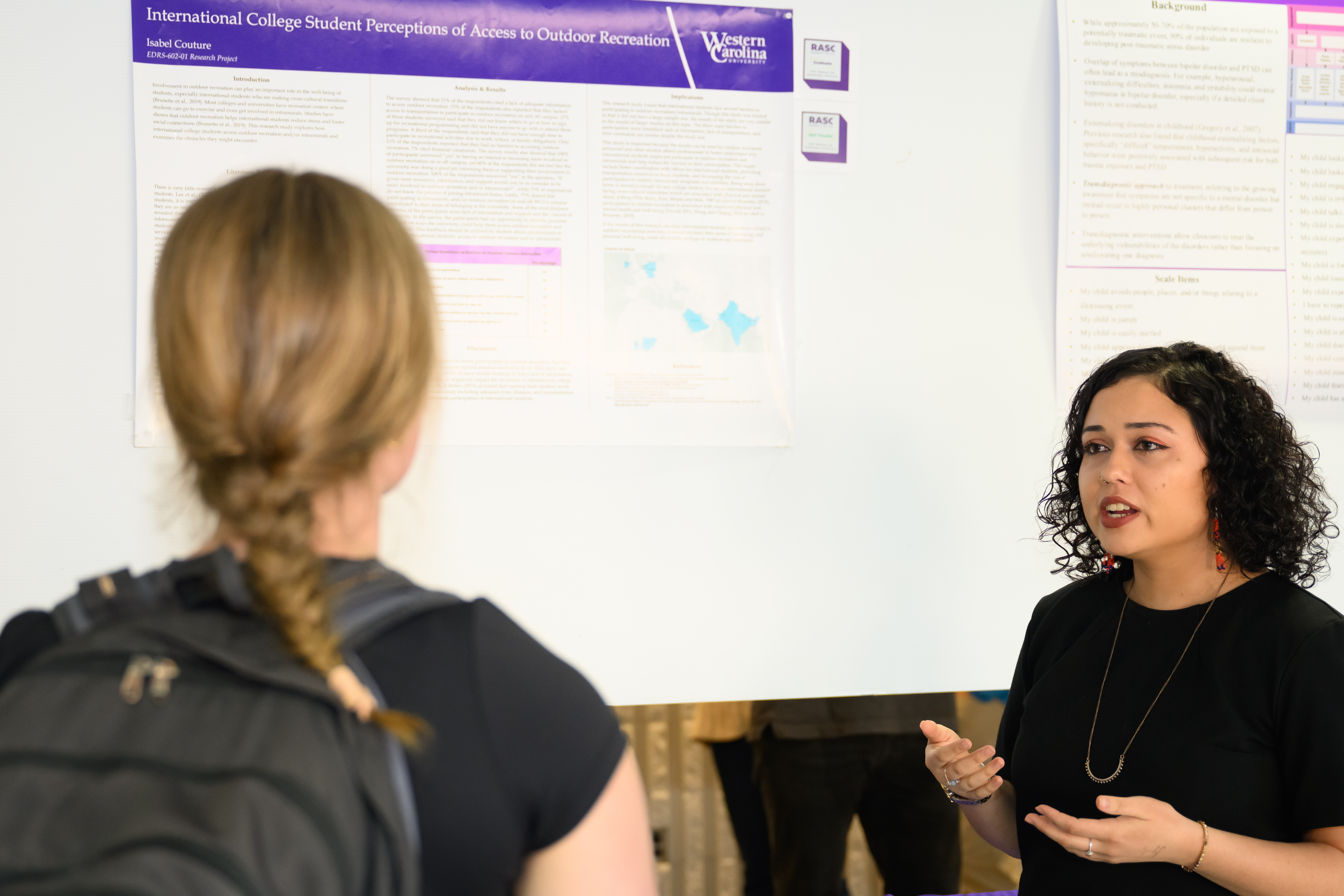 A woman stands in front of her presentation and shares information with an onlooker
