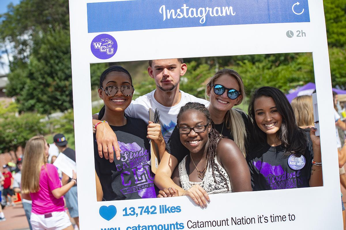 Students hold up a WCU Instagram poster and smile for the camera