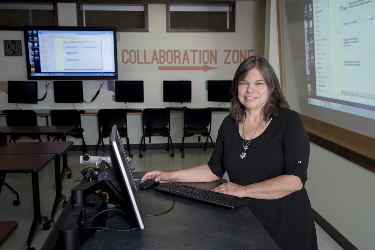 Teacher smiles for the camera at her desk while working at her computer