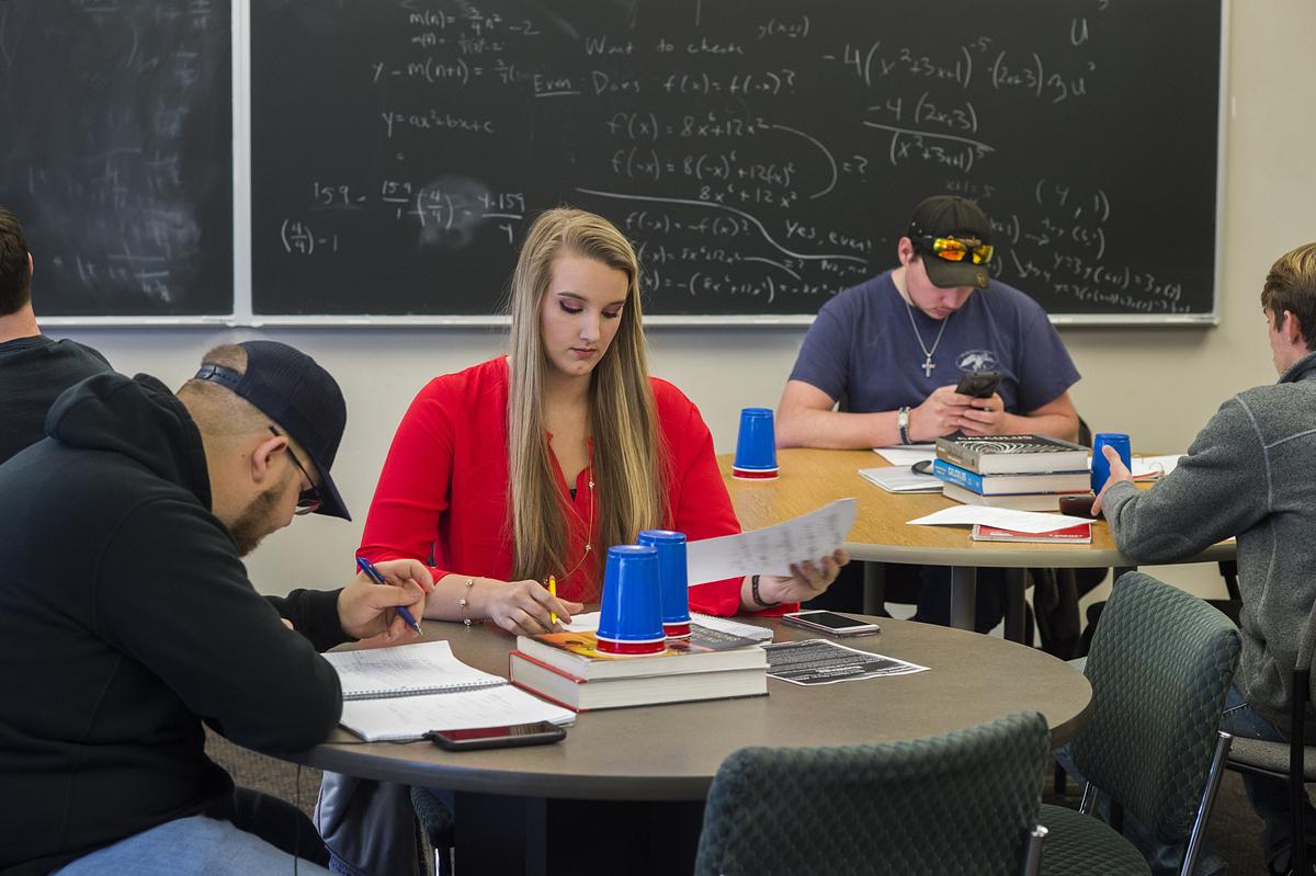 Students working on math equations at various desks in a classroom 
