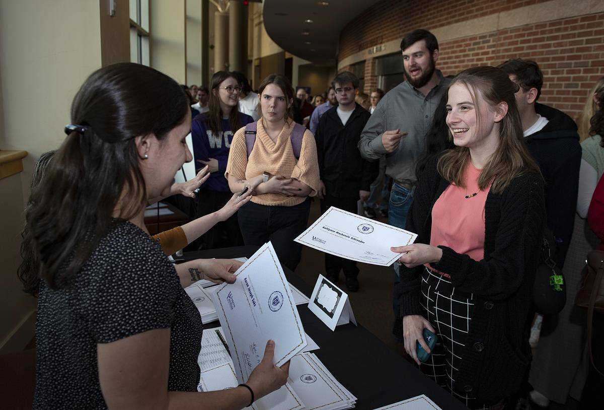 Staff member hands a smiling student her Chancellor's List certificate